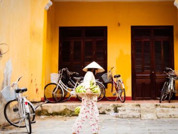 a woman in white walking along a street in front of a yellow building
