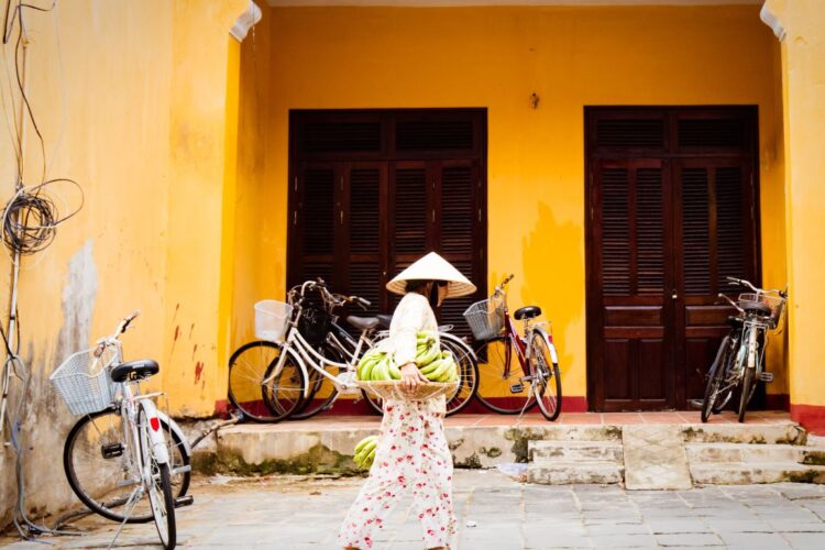a woman in white walking along a street in front of a yellow building