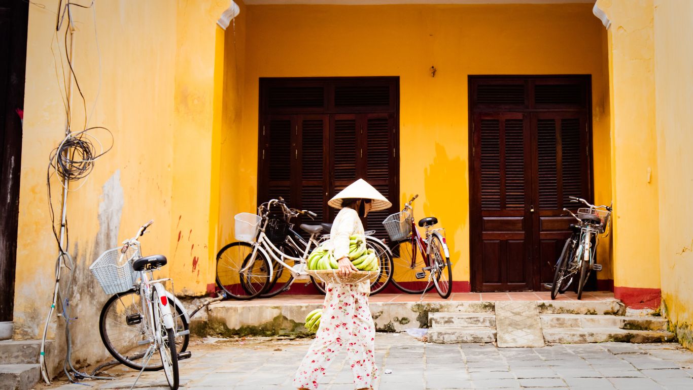 a woman in white walking along a street in front of a yellow building