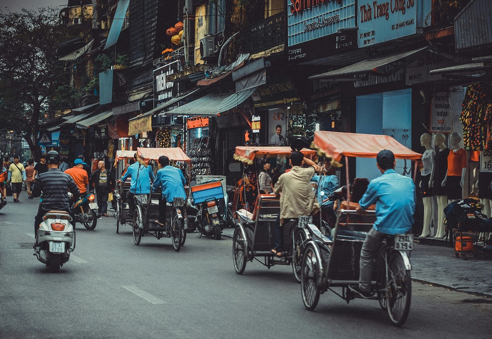 A number of tuk-tuks and motorbikes driving through a busy street